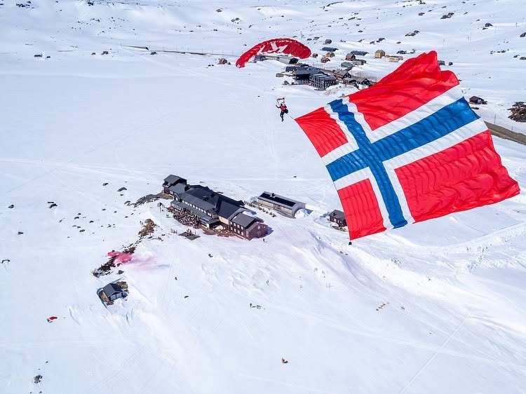 Fallskjermhopper med norsk flagg over et snødekt skiområde
